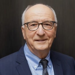 John Willinsky wears black framed glasses, a dark blue suit jacket and tie, with a light blue collared shirt. He smiles thoughtfully at the camera.